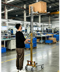 Portable Manual Material Lift With Winch And Forks For Easy Equipment Handling lifting a cardboard box in a factory.