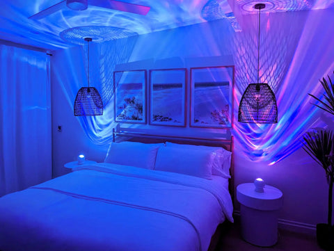LED Aurora Projector With Northern Lights Vibe WiFi App Control Chill Bedroom Relaxation Mood Lighting For Meditation And Home Theater Atmosphere Cozy Night Light Gift creating a calming blue ambiance in a cozy bedroom with framed art and stylish lamps.