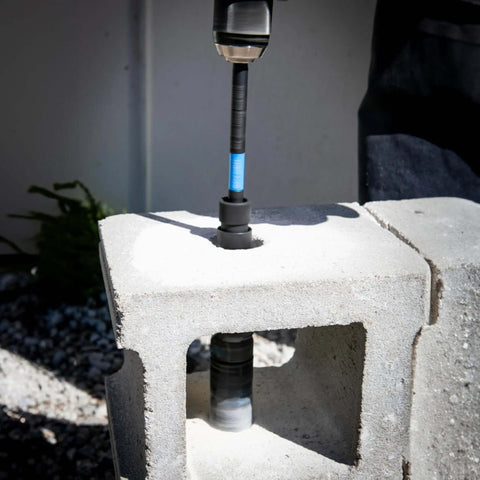 Spyder 12-inch dual-hex locking hole saw extension chuck on a drill with blue band, drilling into concrete block.