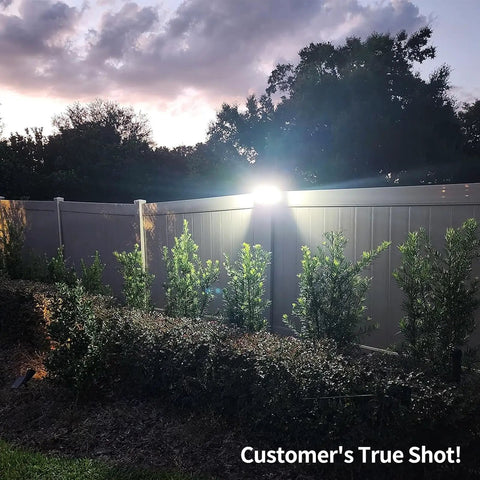 Solar Backyard Flood Lights With 6000mAh Battery illuminating a garden fence at dusk, highlighting surrounding trees and shrubs.