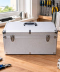 Heavy Duty Silver Metal Tool Box With Reinforced Corners Secure Carry Handle Tough As Nails For Workshop And Field Repair Jobs Keeps All Gear Locked And Loaded on a wooden table with tools.