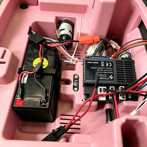 Interior view of ride-on car with 12V JR1922RXS Receiver, 2.4G Bluetooth Remote Control Box Kit, battery, and wiring inside.