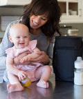 Mom smiling with baby on countertop beside Insulated Baby Bottle Bag And Breastmilk Cooler Keeps Six Milk Bottles Chilled With Ice Pack.