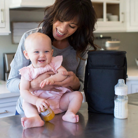 Mom smiling with baby on countertop beside Insulated Baby Bottle Bag And Breastmilk Cooler Keeps Six Milk Bottles Chilled With Ice Pack.