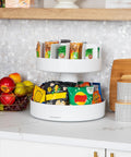 Smooth Rotating Two Tier Snack Carousel Countertop Organizer in white, featuring snacks and fruits displayed elegantly.