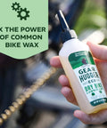 Hand holding Plant Powered Bike Chain Lubricant 3.2 Oz Pack Of 1, Eco Friendly No Teflon No Petroleum No PTFE near a bike chain