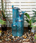 Totally Dope 32 Inch Tall Ceramic Outdoor Water Fountain With Led 4 Tier Tropical Cascading Waterfall Turquoise Glaze Embossed Fern Pattern Bird Attracting Garden Yard Patio Decor on a wooden deck with plants.