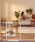 Extra Wide Indoor Baby Gate With Auto Close And Hold Open in doorway, toddler playing, and adult relaxing on sofa in background