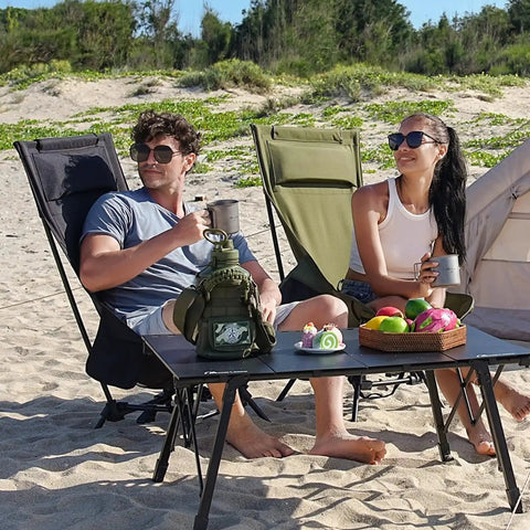 Couple relaxing on beach with High Back Folding Camping Chair With Three-Position Height Adjustment, picnic table in front.