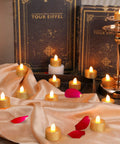 Gold LED Tea Lights Flameless Battery Operated Tealights 24 Pack For Holiday Decor Weddings Parties Birthday Home Ambience Glitter Votive Candles With Easy Cleanup And Safe Realistic Long Lasting Lit Glow arranged on cloth with petals and books.