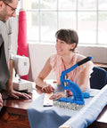 Smiling woman using table mounted eyelet and grommet machine kit with die set, hand press tool, surrounded by fabric and grommets.