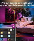 Child relaxing on outdoor sofa with app controlling Lily Outdoor Smart Spotlight Base Kit Three Pack With White And Color Ambiance LED Walkway Lights For Low Voltage Landscape Lighting No Fuss Setup Bridge Required Control With App And Voice Weatherproof.