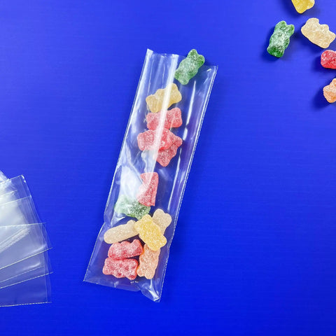 Clear Flat Open Poly Bags 2x6 Inch 1.25 Mil Pack Of 100 For Easy Packing, Shipping And Storage, Food Safe And FDA Compliant Poly Bags That Keep Items Fresh And Organized. Clear poly bag holding gummy candies on blue background