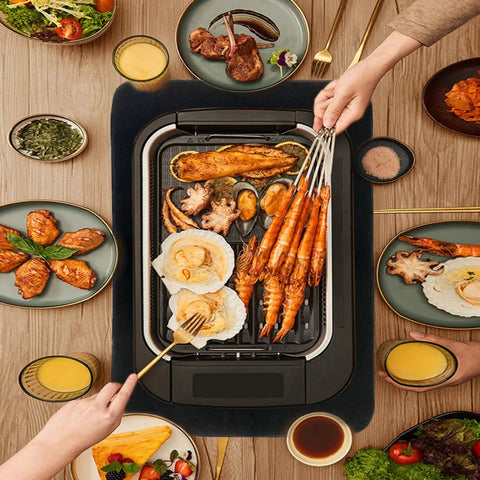 Top view of a table with assorted grilled seafood and steak, hand holding skewers over a grill surrounded by various dishes.