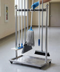 Go-To Floor Standing Mop And Broom Storage Rack For Schools, Factories, And Maintenance Crews - Heavy-Duty Cleaning Tool Holder, Movable Organizer, Keeps Cleaning Supplies Neat, Accessible, Ready To Use. Stainless steel floor-standing rack on casters holding mops and brooms.