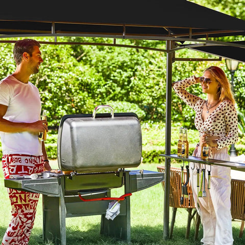 Outdoor scene with 5x8 Grill Gazebo With Extra Shade Awning Party Ready Vibe All Weather Steel Frame Double Tier Canopy Roof Sturdy Metal Serving Shelves Built In LED Lights Bottle Opener Patio Backyard BBQ Shelter Black, showing two people enjoying a barbecue.