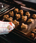 Baker placing cookies on Extra Thick 18 By 14 Inch Aluminum Cookie Sheet With Hanging Hole Large Flat Baking Pan 2.7mm Thick Pro Grade.