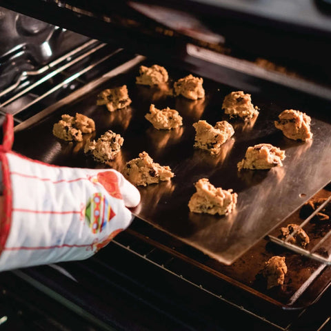 Baker placing cookies on Extra Thick 18 By 14 Inch Aluminum Cookie Sheet With Hanging Hole Large Flat Baking Pan 2.7mm Thick Pro Grade.