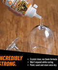 Gorilla Glue bottle dispensing crystal-clear adhesive onto the stem of a wine glass on a wooden table.