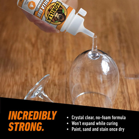 Gorilla Glue bottle dispensing crystal-clear adhesive onto the stem of a wine glass on a wooden table.