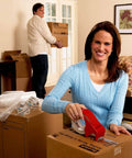Woman using portable heavy-duty packaging tape dispenser with hand brake for 3 in core rolls up to 2 in wide in a living room setting.