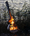 Guitar Shaped Outdoor Fire Pit Stainless Steel Wood Burning With Removable Ash Pan, lit at twilight by lakeside.