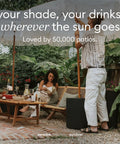 Outdoor scene with two people enjoying a patio with Durable Outdoor Umbrella Side Table With Umbrella Hole Package visible.