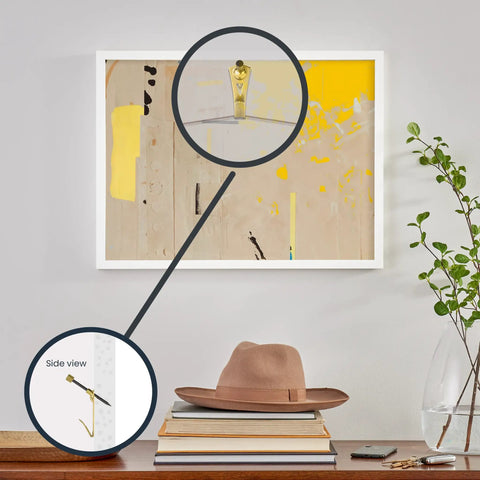Wall Safe Pro Picture Hanger Set With Brass Padded Hooks shown mounting art above a bookshelf, close-up of hook detail