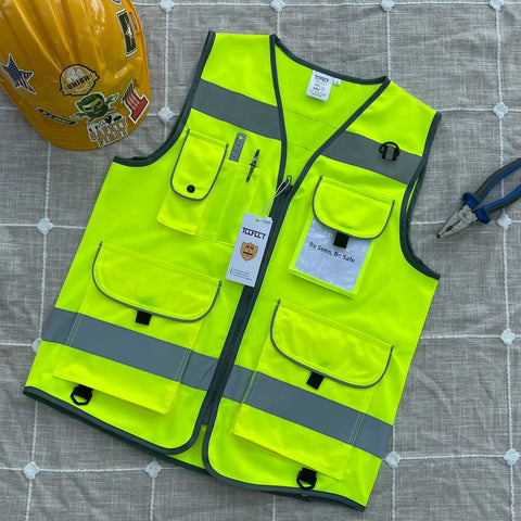 High Visibility Safety Vest For Men And Women With 9 Pockets, Reflective Strips For 360 Degree Night Visibility, ANSI ISEA Approved Work Vest In Yellow, X Large on a table with helmet and pliers