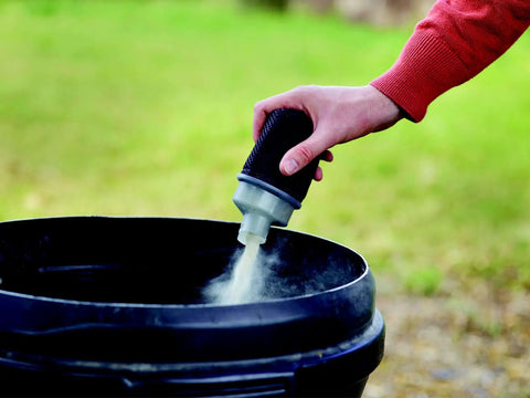 Hand holding a dusting tool above a black bucket, releasing fine powder for woodworking, showcasing the Quarter Sheet Orbital Palm Sander Professional Grade 220 Watt Motor Featuring A Snappy Pressure Trigger Switch Lightweight Orange Body Crushes Tough Woodwork Jobs Quickly To Leave Surfaces Smooth As Silk Daily.