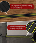 Black 6 Ft Floor Cable Cover With Three Large Cord Channels, anti-slip texture, and yellow warning lines on wooden and tiled floors.