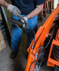 Person using All In One Grease Fitting Tool For 1/8 And 7/16 NPT on an orange tractor in a garage setting.
