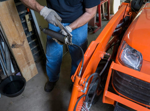 Person using All In One Grease Fitting Tool For 1/8 And 7/16 NPT on an orange tractor in a garage setting.