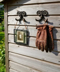 Heavy Duty Kickass Cast Iron Mustache Wall Hooks holding leather gloves and a framed photo on wooden wall outdoors.