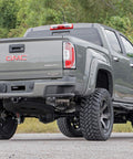 GMC pickup truck, gray, lifted with oversized off-road tires and riveted fender flares, rear three-quarter view.