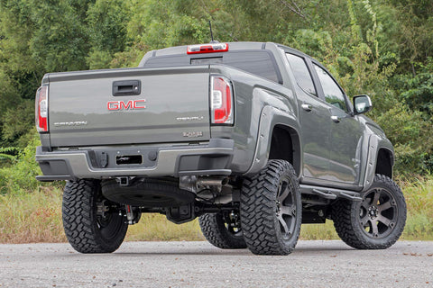 GMC pickup truck, gray, lifted with oversized off-road tires and riveted fender flares, rear three-quarter view.