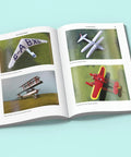 Open book showing "Conversions and Scratchbuilding Masterclass for Aircraft Modeling with Hands On Pro Tips and Superdetailing Weathering for Builders to Elevate Your Plastic Aircraft Projects" with model planes images.