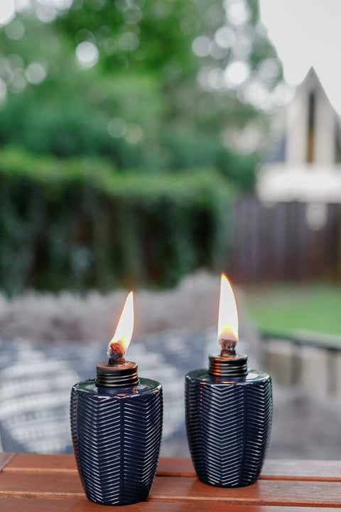 Glass Table Torch Set For Outdoor Patio Vibe, Herringbone Blue 3-Pack lit on patio table with green background