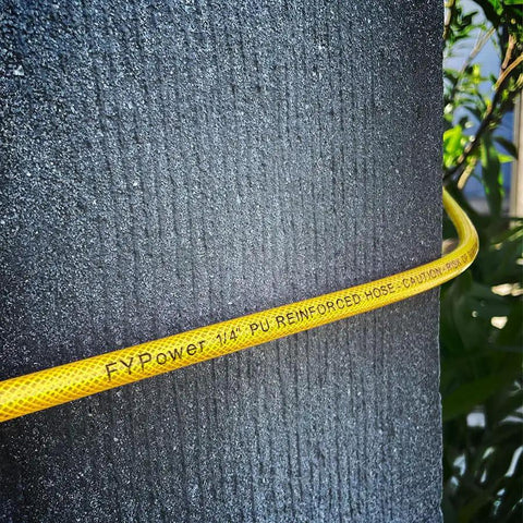 Badass 1/4 Inch By 100 Feet Air Compressor Hose Crafted From Tough Reinforced Polyurethane, coiled around a textured wall.