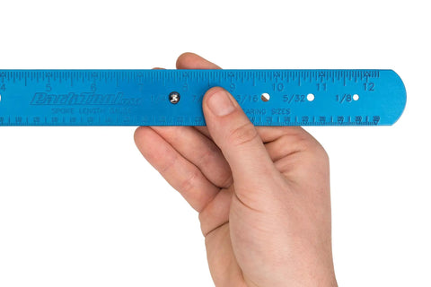 Close-up of hand holding Spoke Bearing And Cotter Gauge For Bicycles, Handy Wheel Maintenance Tool with easy-to-read scale.