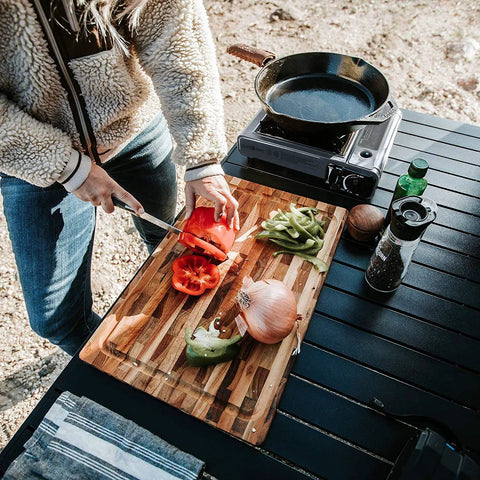 Person preparing vegetables beside a portable butane camping stove with case auto ignition and precise heat control for camping and tailgating