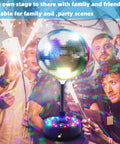 Six Inch Rotating Mirrors Disco Ball Light With Adjustable Five To Nine RPM Motor Base 24 RGB LED Mood Lights USB Or Battery Powered Lit For Party Club Stage Dance Bar with colorful reflections at a party.