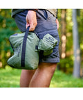 Person carrying Pre Filled All Weather Rifle Sandbag Rest For Bench Shooting And Competition Front And Rear Set Ready To Use Heavy Duty 900D Oxford Fabric Tear Resistant Olive Drab in outdoor setting.