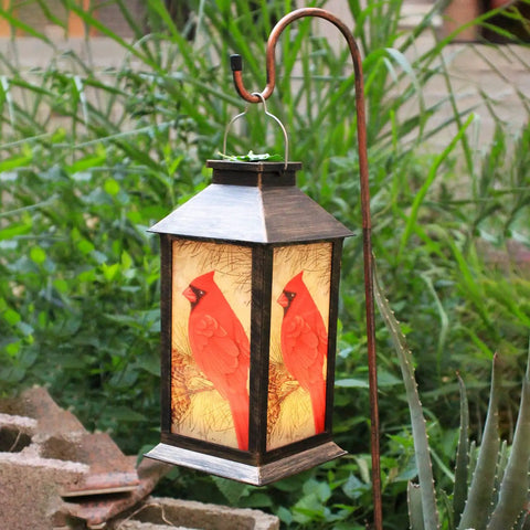 Outdoor Solar Lanterns For Hanging And Tabletop Use Waterproof LED Red Cardinal Bird Pattern Lights With S Hook Ideal Patio Garden Decor And Thoughtful Gift For Mom Grandma Women hanging on a stand in a garden.