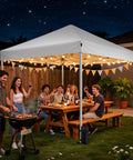 10x10 Pop Up Canopy Tent With Instant One Button Setup Carry Bag Four Sandbags And Eight Stakes Lightweight Outdoor Shade For Parties, Camping, Markets And Events White in a backyard at night with people enjoying a meal.