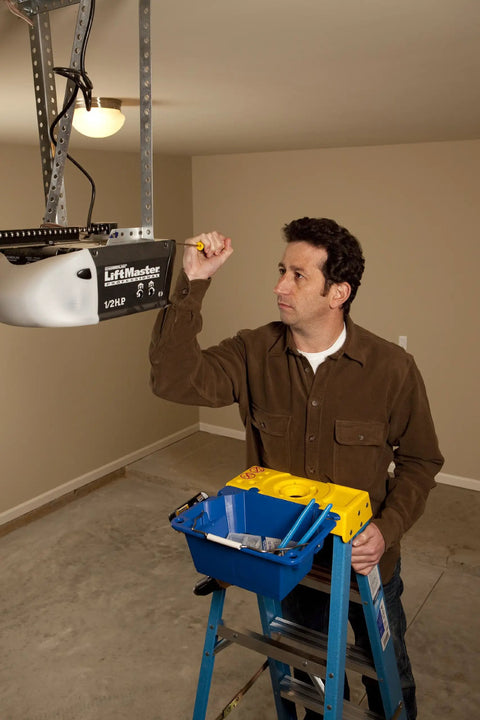 Man using AC52-UB Ladder Accessory Kit With Liquid Holder Swiveling Handle on a ladder fixing ceiling garage opener.