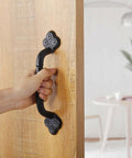 Hand holding Rustic Gate Handle 9 Inch Cast Iron Barn Door Handle on wooden door, black finish, indoor use.
