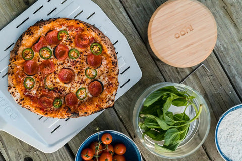 Freshly cooked pizza on 14 Inch Perforated Pizza Peel With Long Handle Aluminum Lightweight Pizza Paddle, surrounded by ingredients.