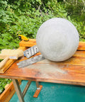 16 Inch Concrete Orb Mold For Garden Decor Durable Reusable Plastic Ball Mold For DIY Cement Stones And Spheres Great For Outdoor Landscaping And Patio Projects; finished cement sphere on wooden table outdoors with tools in view.