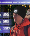 Man wearing Rechargeable LED Beanie With Built In Light, USB Powered Winter Knit Hat, adjusting brightness settings, outdoor use.